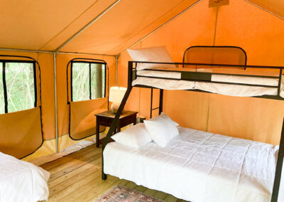 glamping tent interior with bunk bed cozy linens warm lighting and wood floor perfect for luxury camping retreats