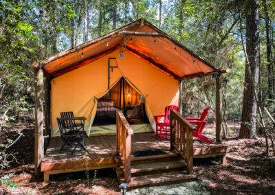 glamping tent in forest setting with wooden deck chairs cozy interior nature retreat
