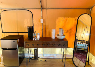 glamping tent interior with mini fridge coffee maker wooden table and mirror cozy rustic luxury accommodation