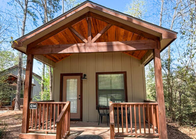 Wood cabin porch, forest retreat, nature getaway, rustic design, cozy accommodation, tranquil setting, outdoor relaxation.