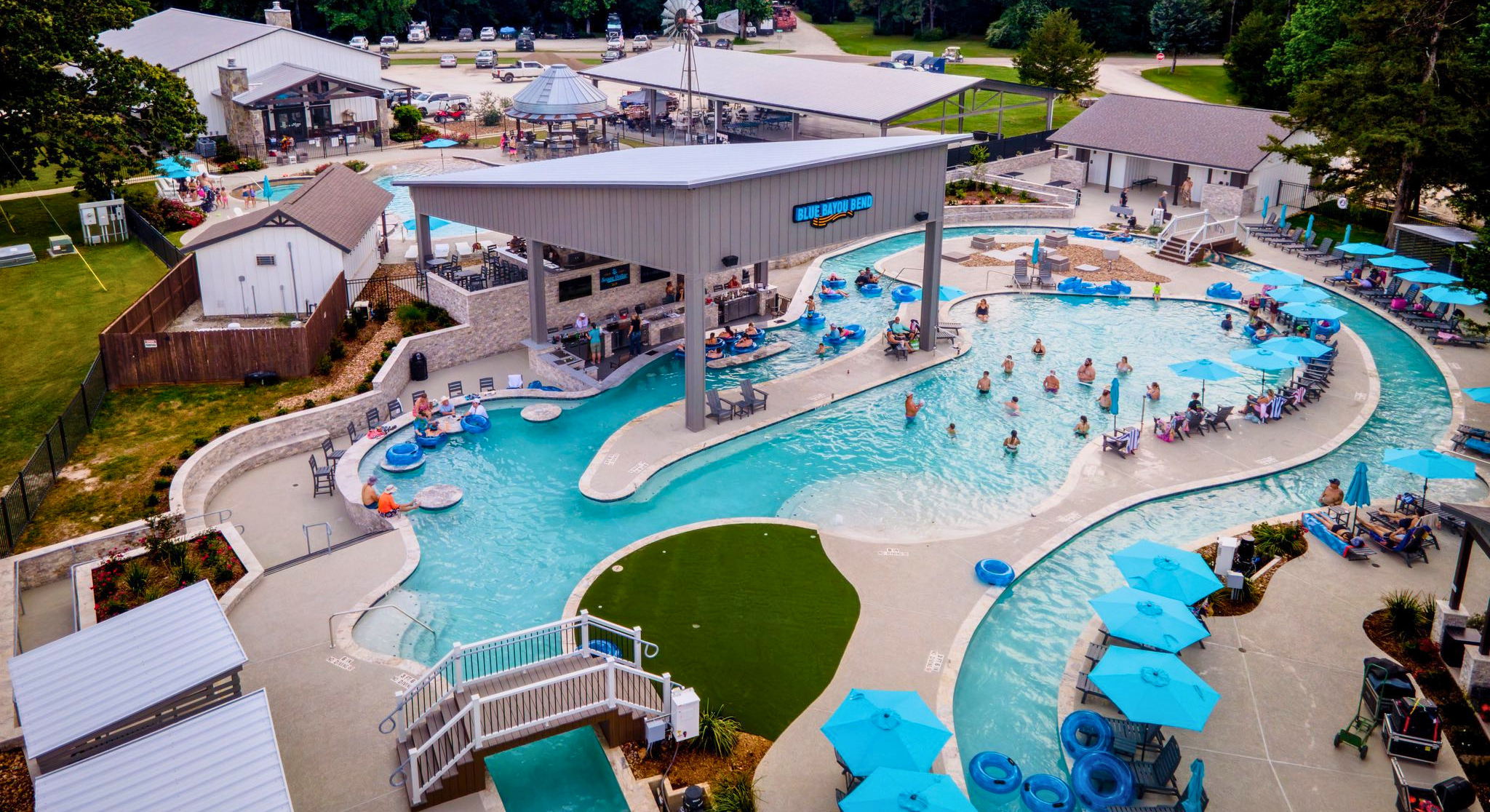 Aerial view of a vibrant pool area with lazy river, blue umbrellas, and happy guests.