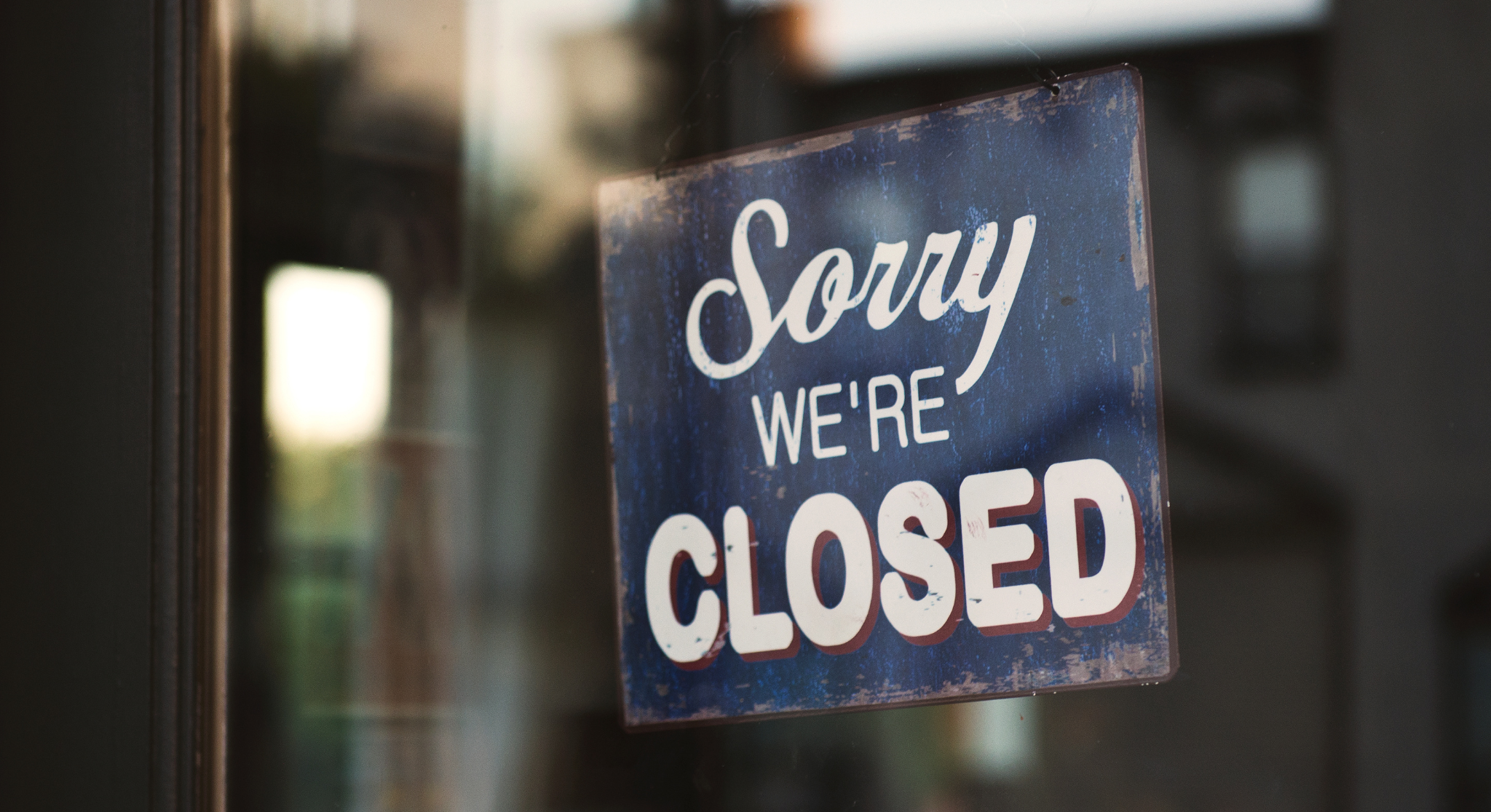 Blue, weathered sign reading 'Sorry we're closed' hanging in a storefront window