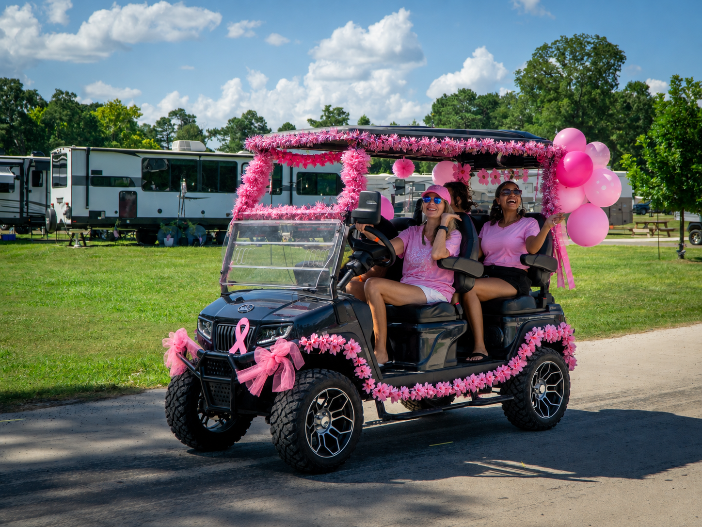 pink-out-weekend-golf-cart-two-creeks-crossing-resort Pink decorated golf cart with pink flowers, ribbons, and balloons, carrying two smiling women in pink shirts on a sunny day festival scene.
